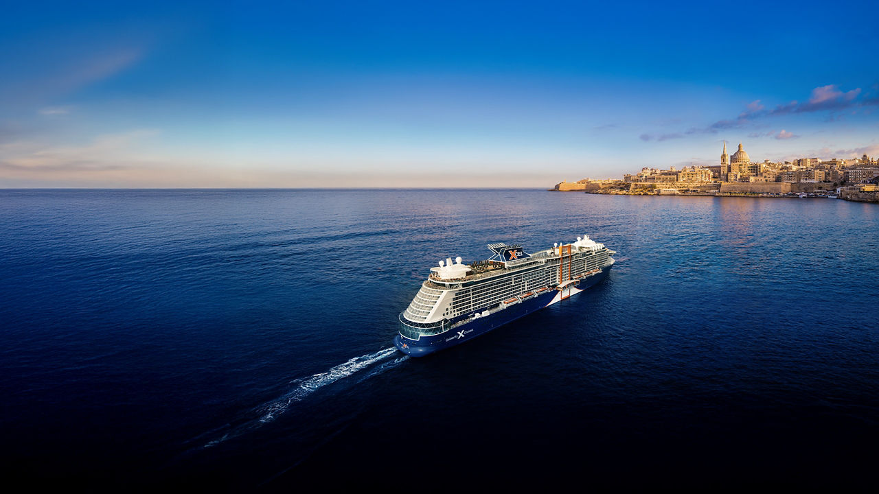 Celebrity Xcel in Alaska  traveling across calm ocean water at sunset with coastal hills in the distance