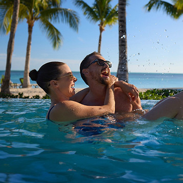 A person standing on a cruise ship deck photographing a glacier and icy blue water with rocky mountains in the background.