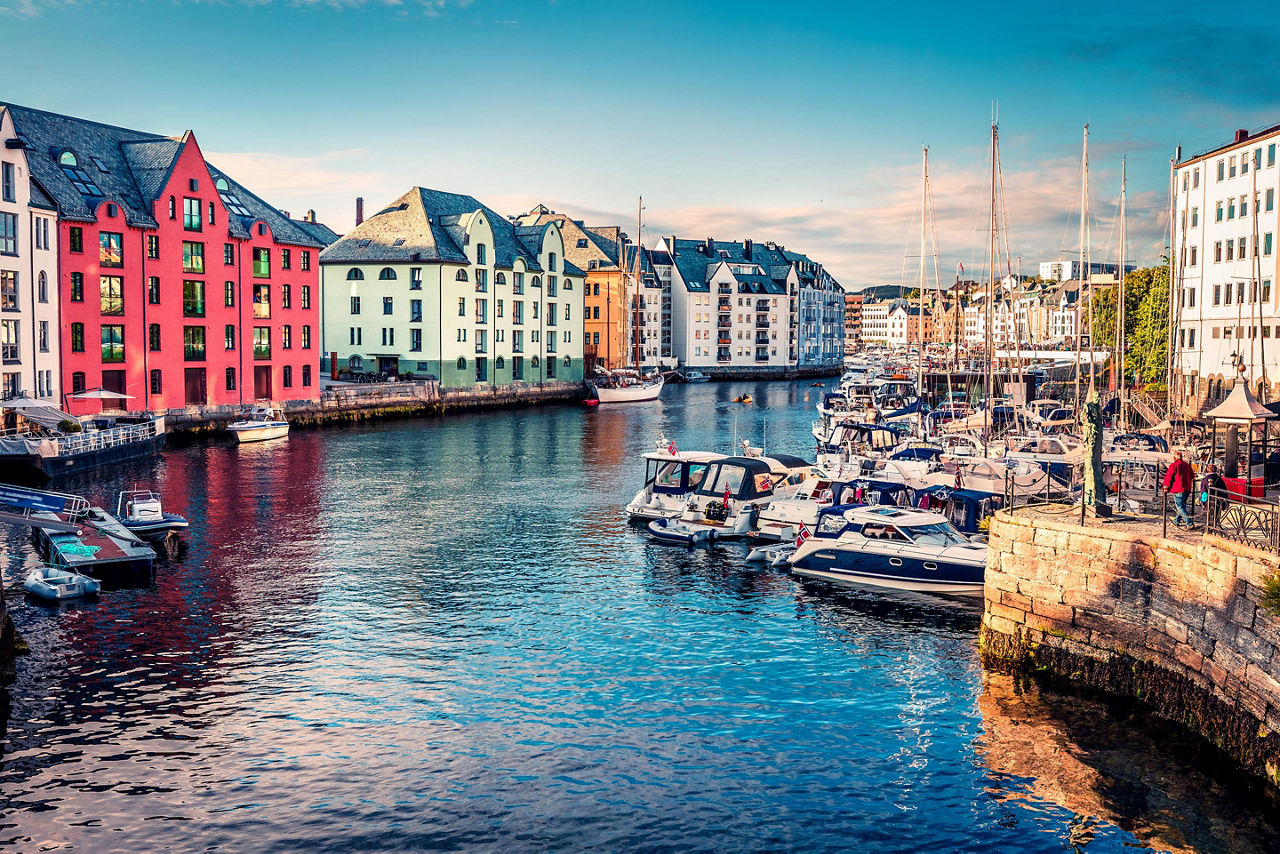 Boats docked in a river in Alesund, Norway with colorful buildings on the shore
