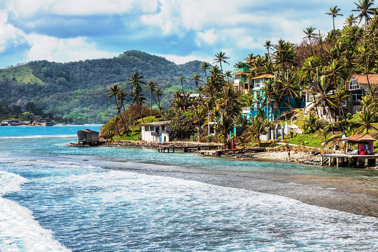 View at Palm trees, sea and houses in Isla Grande shore. Colon province, Panama
