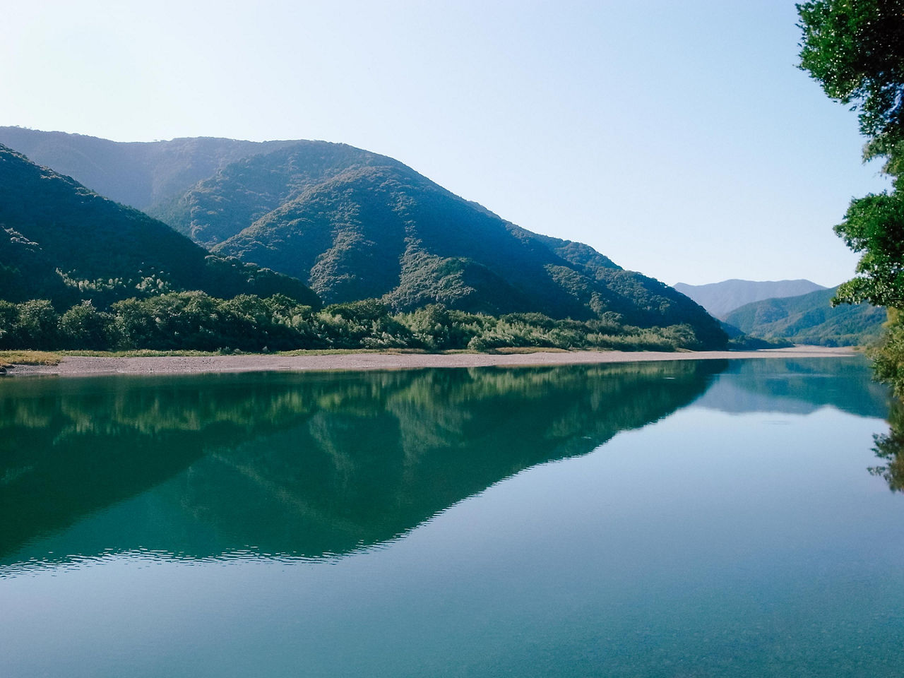 Calm and flat stream with a view of the mountain reflected on the water in the Shimanto River in Kochi, Japan