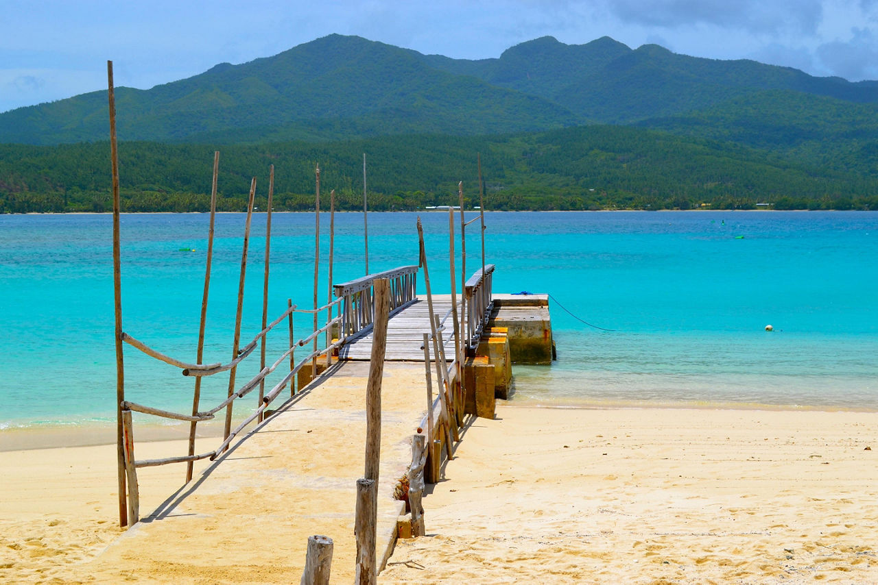 The beach with a make shift dock on the shore with views of mountains in Mystery Island, Vanuatu
