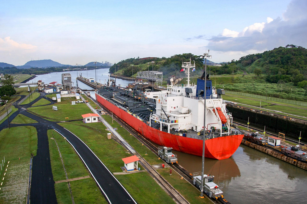 An industrial red ship entering the Panama Canal waterway that connects the Atlantic Ocean to the Pacific Ocean