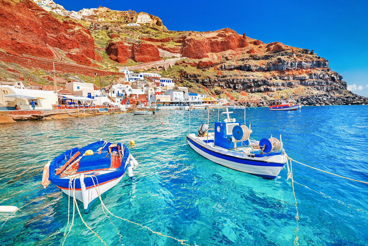 Beautiful landscape of two fishing boats anchored in blue water at the old port in Oia, Santorini, Greece