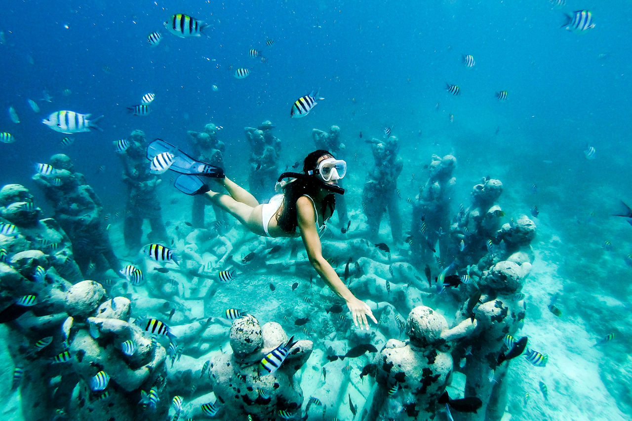 Snorkel woman swimming in a turquoise ocean under the flooded statues