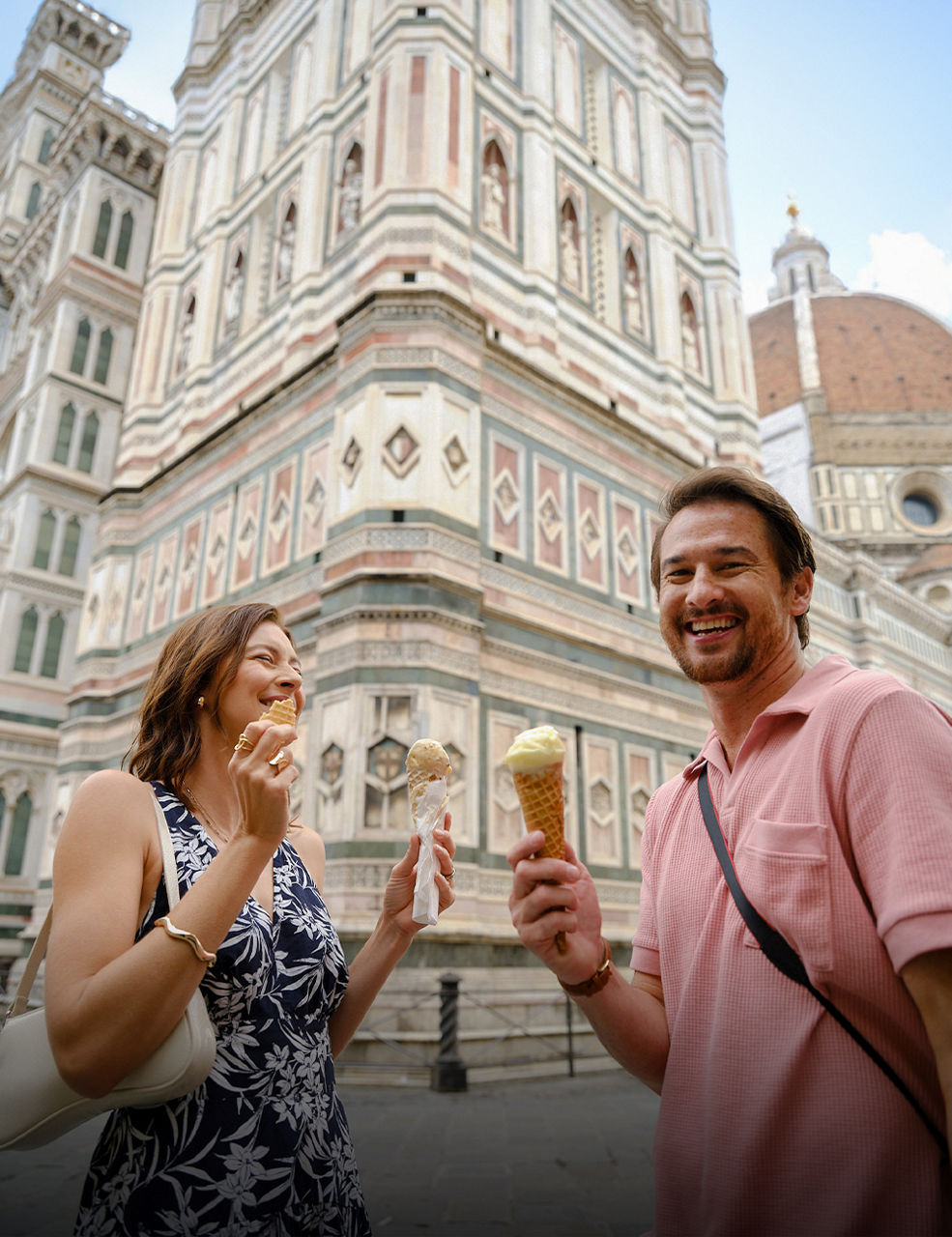A person walking down a whitewashed pathway overlooking the blue‑domed buildings of Oia, Santorini, with views of the Aegean Sea.