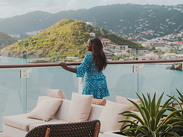  A woman standing on a cruise ship terrace overlooking a coastal town and harbor.