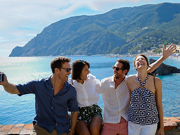 A group of four people sitting on a stone wall beside the sea with the cliffs and villages of Cinque Terre.