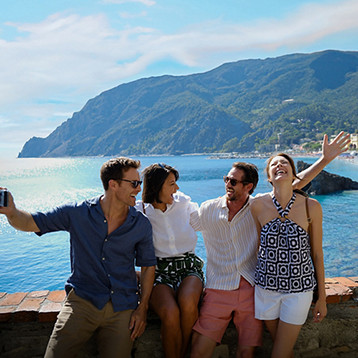 A group of four people sitting on a stone wall beside the sea with the cliffs and villages of Cinque Terre.