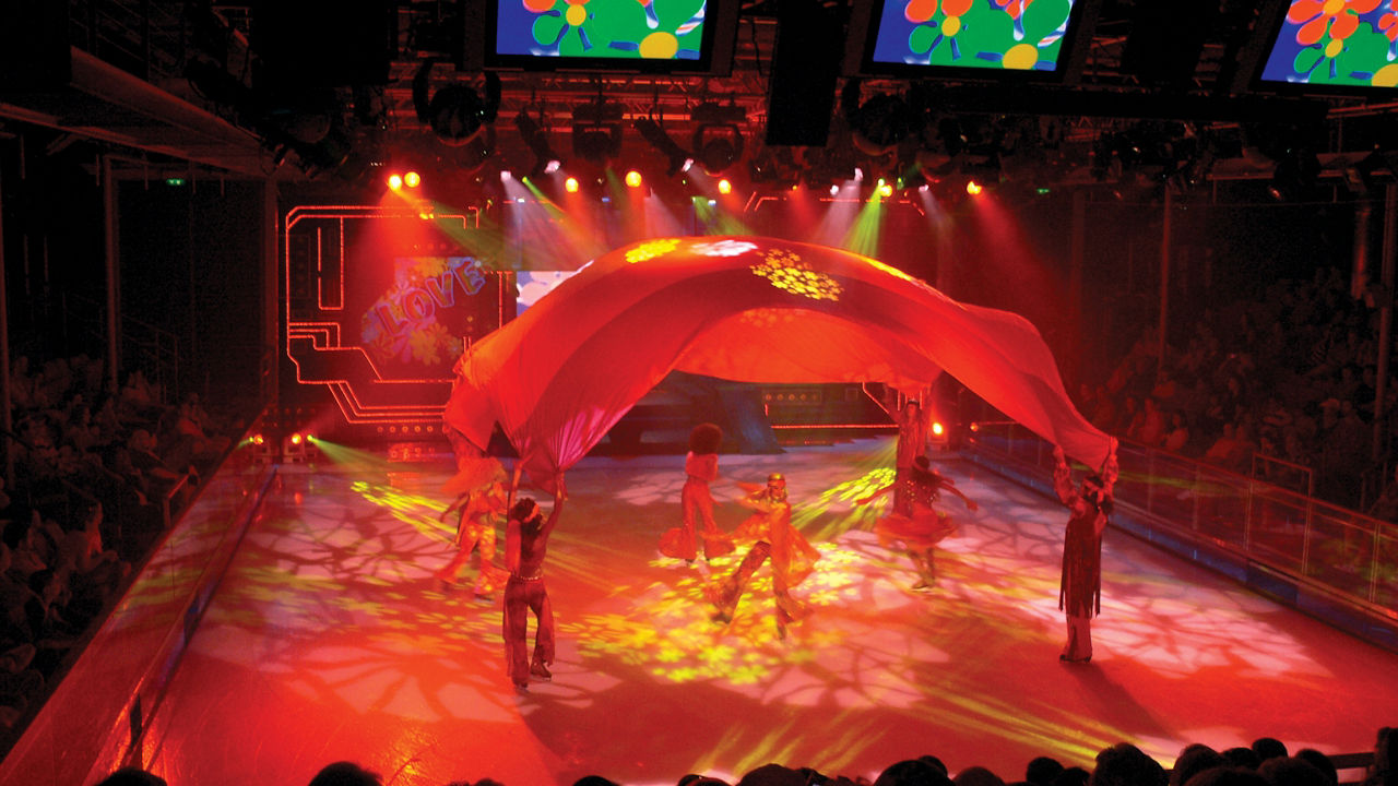 Performers skating under a tent with bright red lights during ice skating shows onboard.