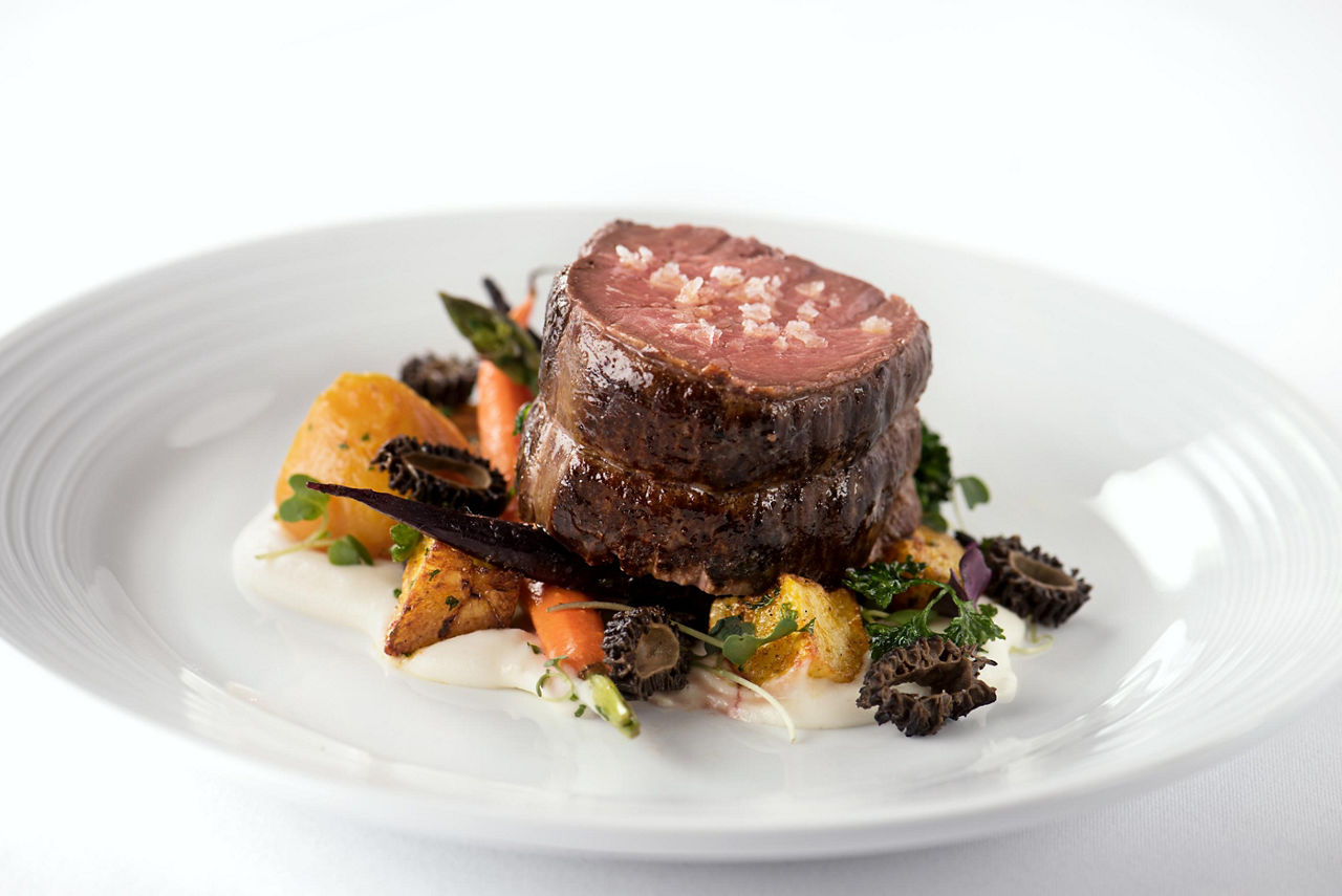 Two slices of steak topped with sea salt served with a side of vegetables at the Main Dining Room