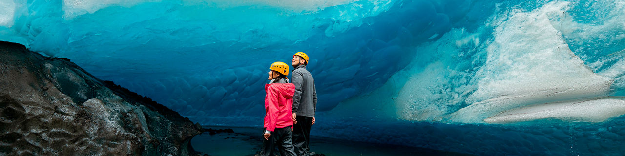 Couple standing on rocky area looking up into glacier, Alaska, Juneau