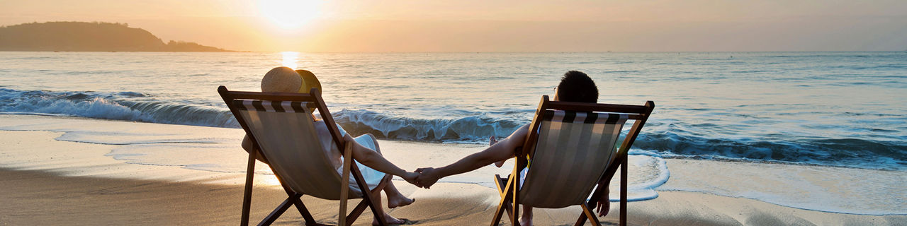 couple sitting in beach chairs on hold hands in front of a sunrise. The Caribbean.