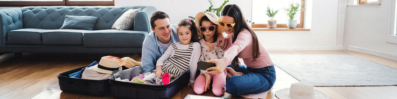 Parents with small daughters indoors at home, packing for summer holiday.