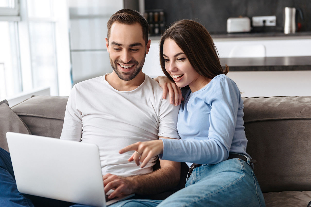 happy couple using laptop, woman pointing.