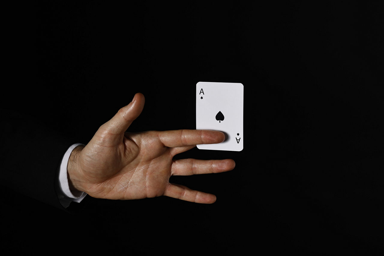 Illusionist with playing card on black background, closeup