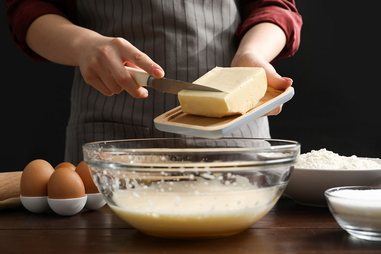 Making cookies. Woman adding butter into dough at table, closeup