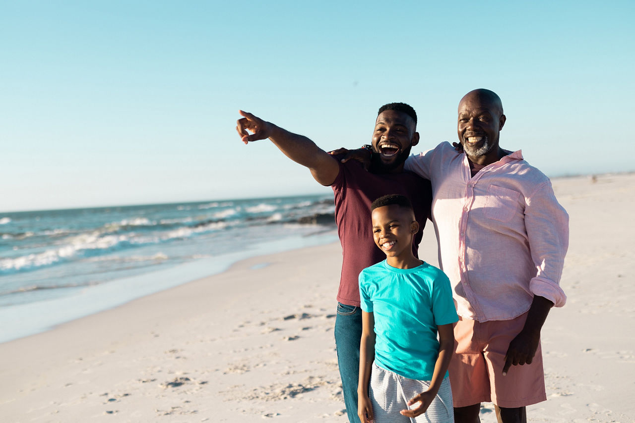 African american male multigeneration family looking away while standing at beach under sky. 
