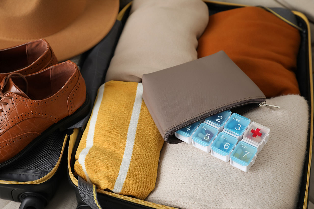 open suitcase with packed clothes accessories and pill box