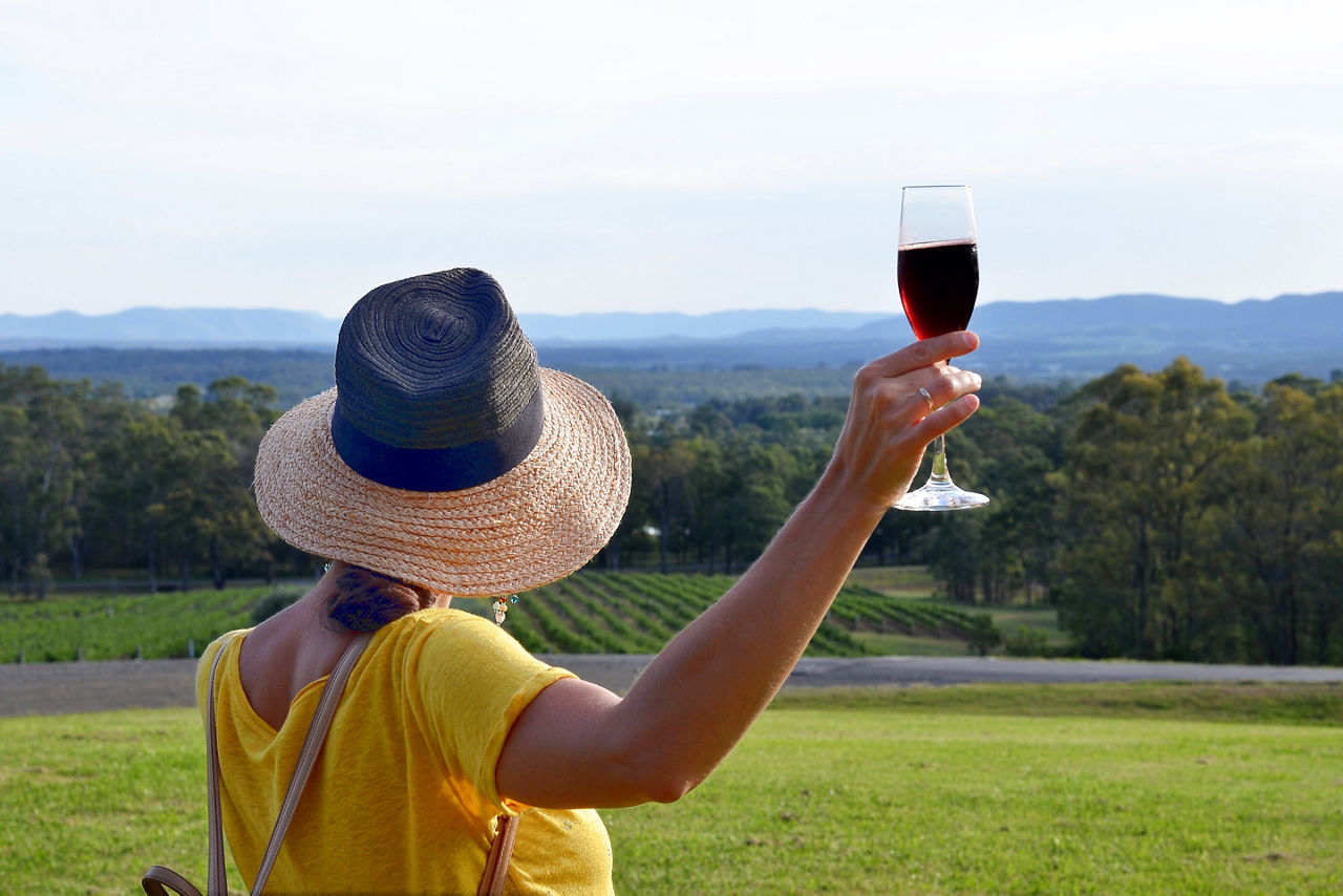 A woman holding a glass of red sparkling wine admiring a beautiful landscape of winery fields, Hunter Valley