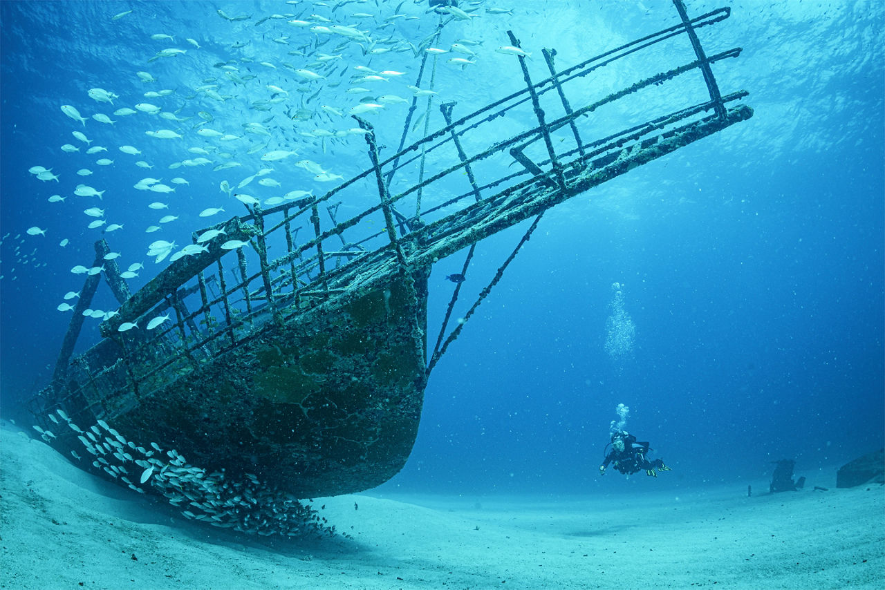 Scuba divers swimming in front of a shipwreck. The Caribbean.