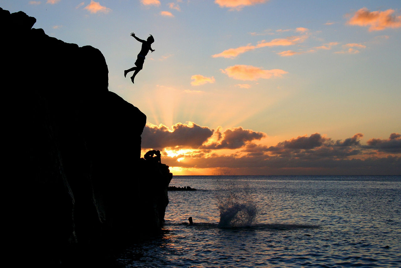 Boy Jumping off a cliff into the ocean at Waimea Bay. Hawaii