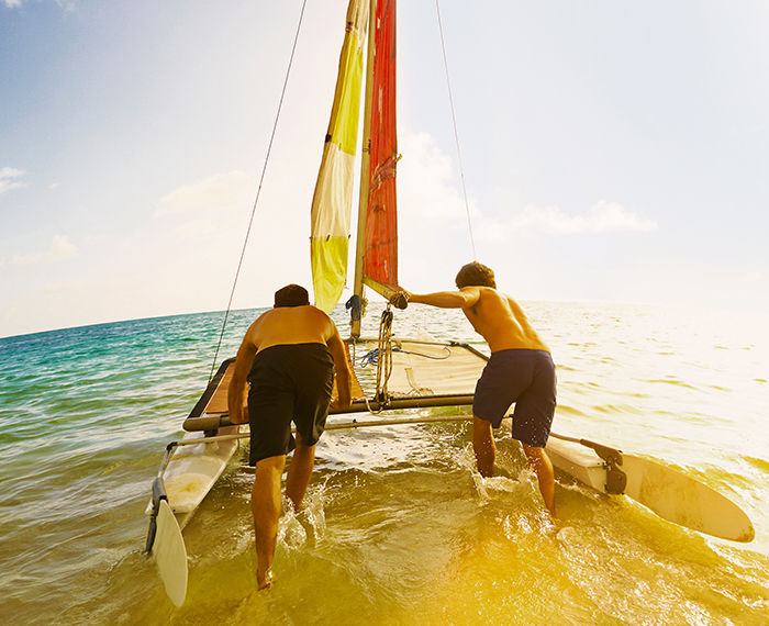 Two friends pushing a sailing boat in the water during cruise vacation.