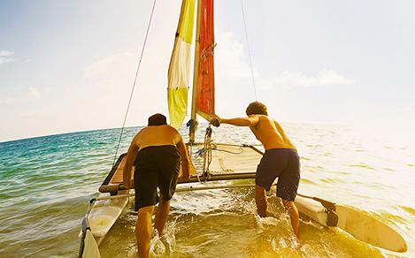 Two friends pushing a sailing boat in the water during cruise vacation.