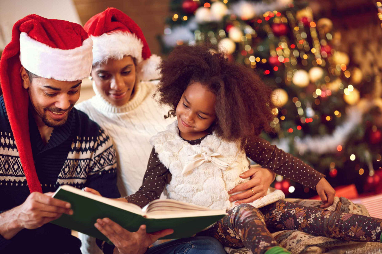 Family wearing Santa Hats Reading a Story with Christmas Tree in the Background