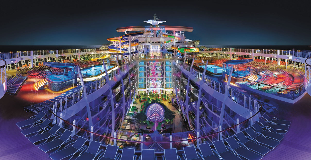 HM, Harmony of the Seas, OOH, wide panoramic view of top deck with the Perfect Storm water slides in center, night, nighttime, top deck with pools, Central Park below, night sky in background, purple, blue colors,