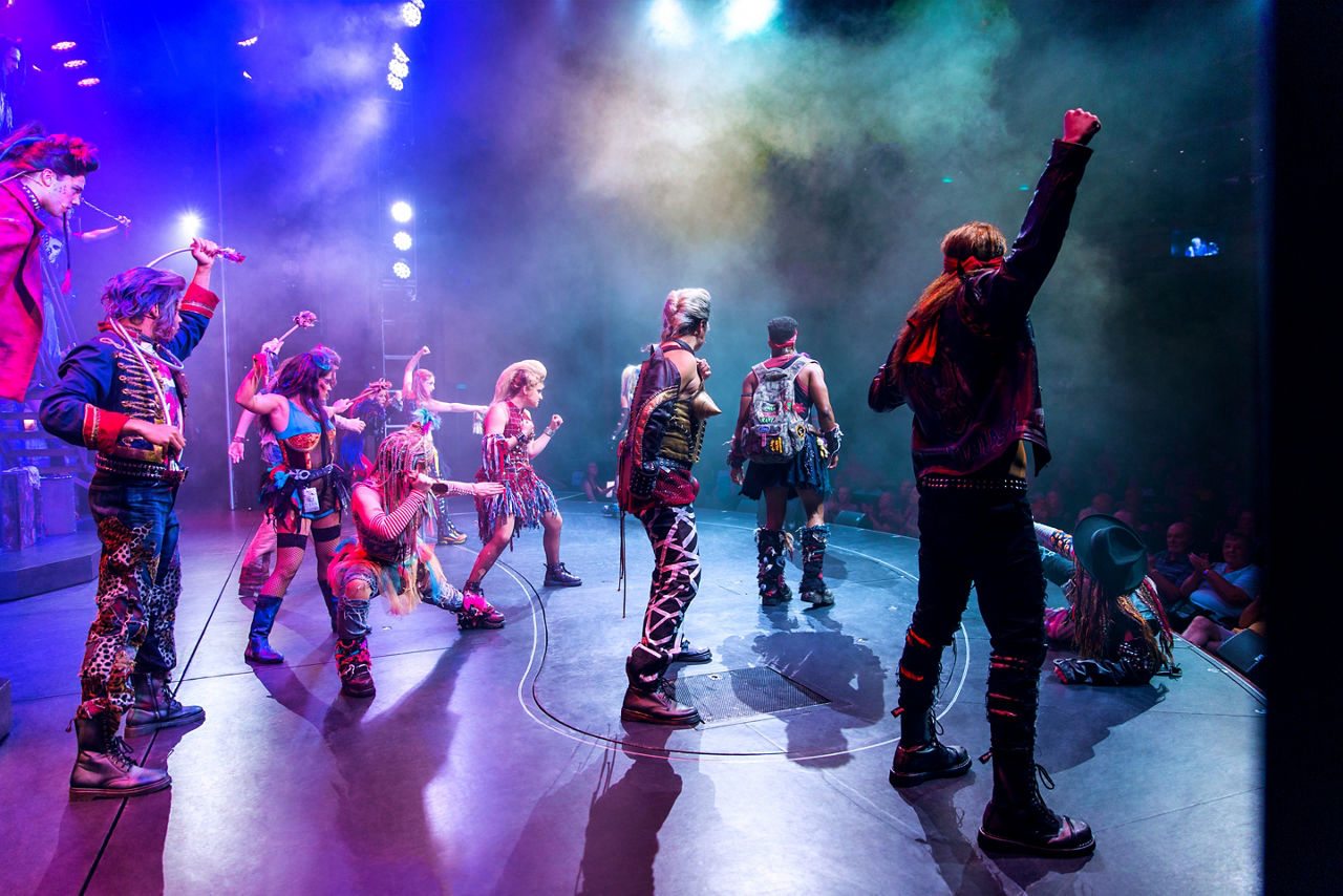 A gang of rockers on stage with their fists up during a We Will Rock You broadway show on a cruise.