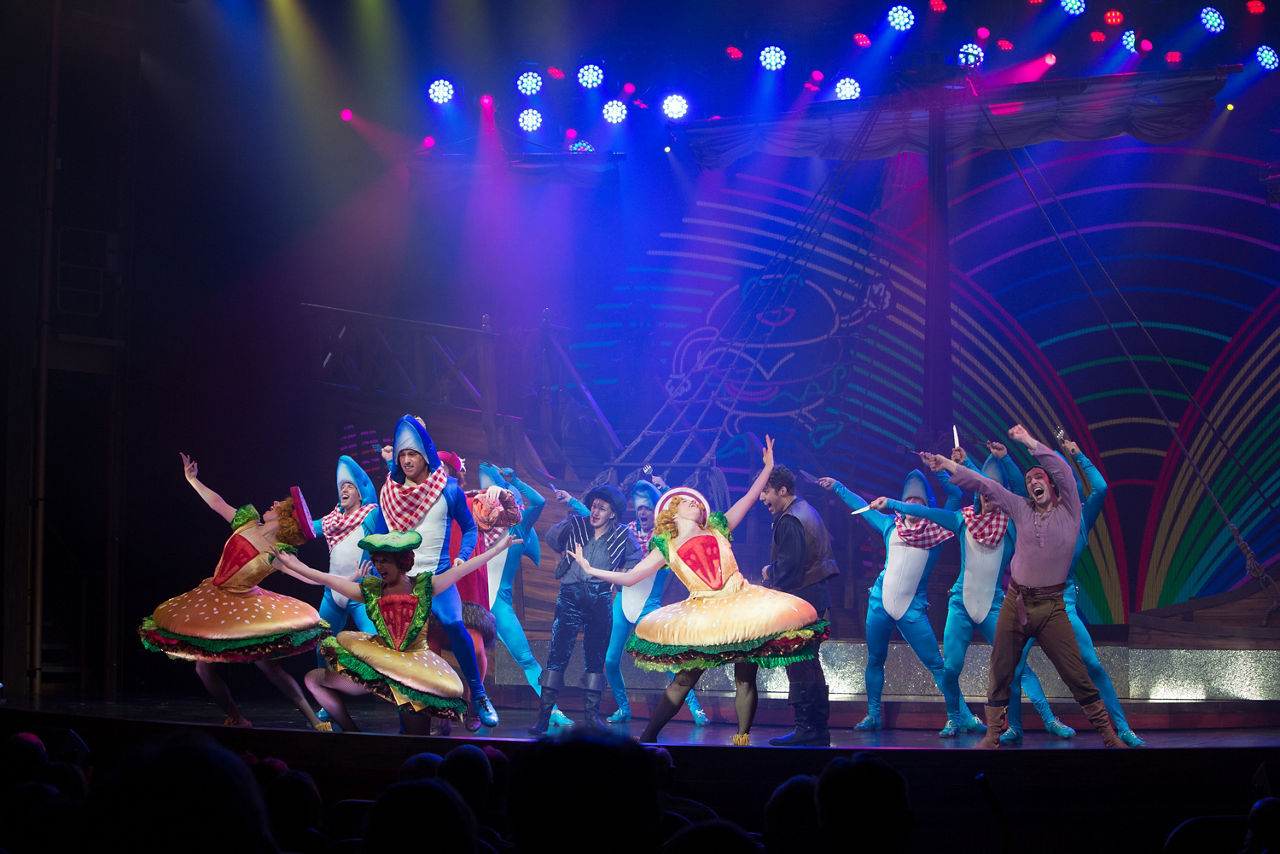 Performers on stage dressed as hamburgers and sharks dancing during the Columbus Musical Cruise Show by Royal Caribbean