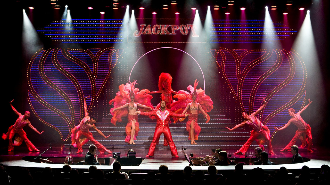Performers in red costumes on stage during the Jackpot Cruise Show on Adventure of the Seas