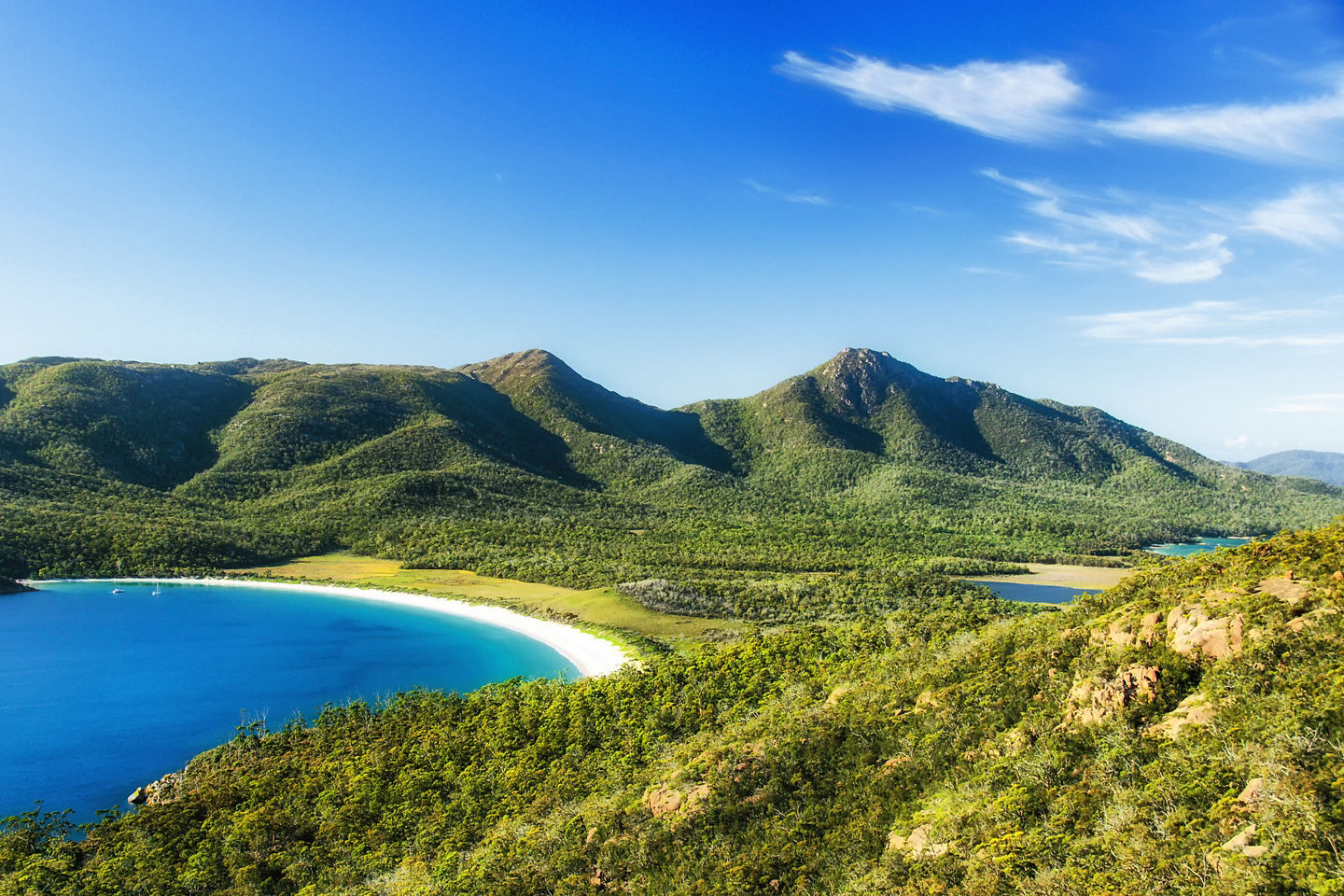 Wineglass Bay with curved white beach, turquoise water, and forested hills.