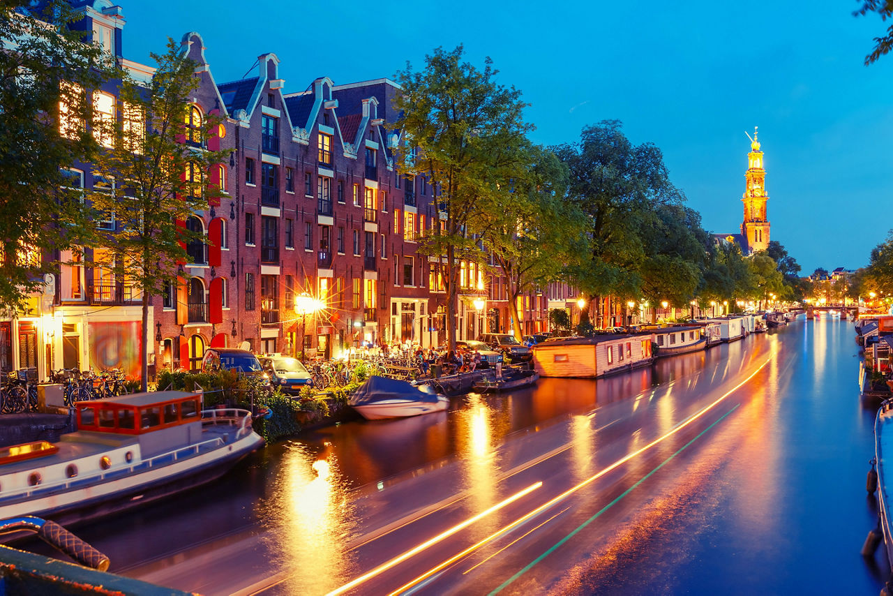Night city view of Amsterdam canal Prinsengracht with houseboats and Westerkerk church and luminous track from the boat