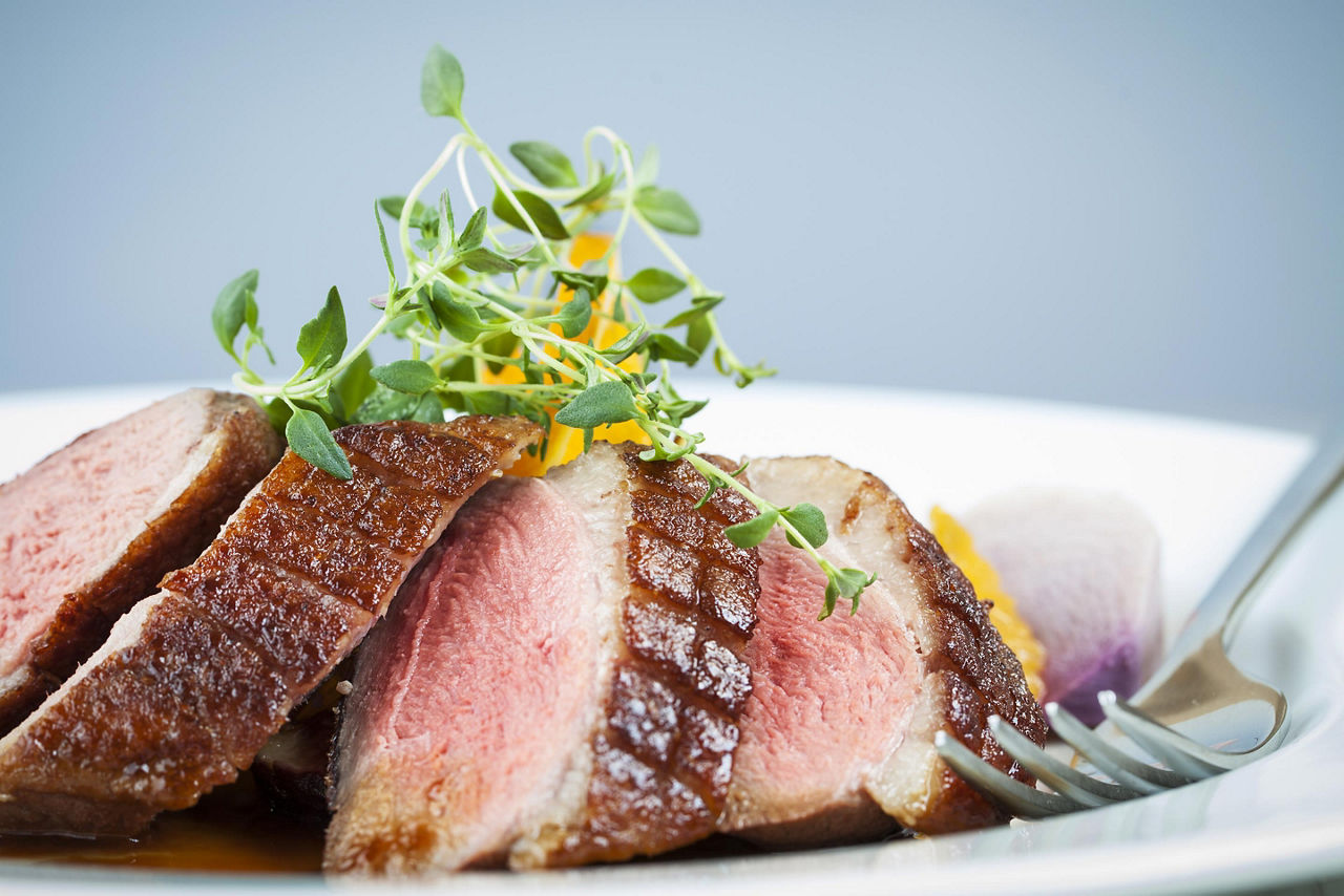 Sliced duck breast on a white plate with a fork