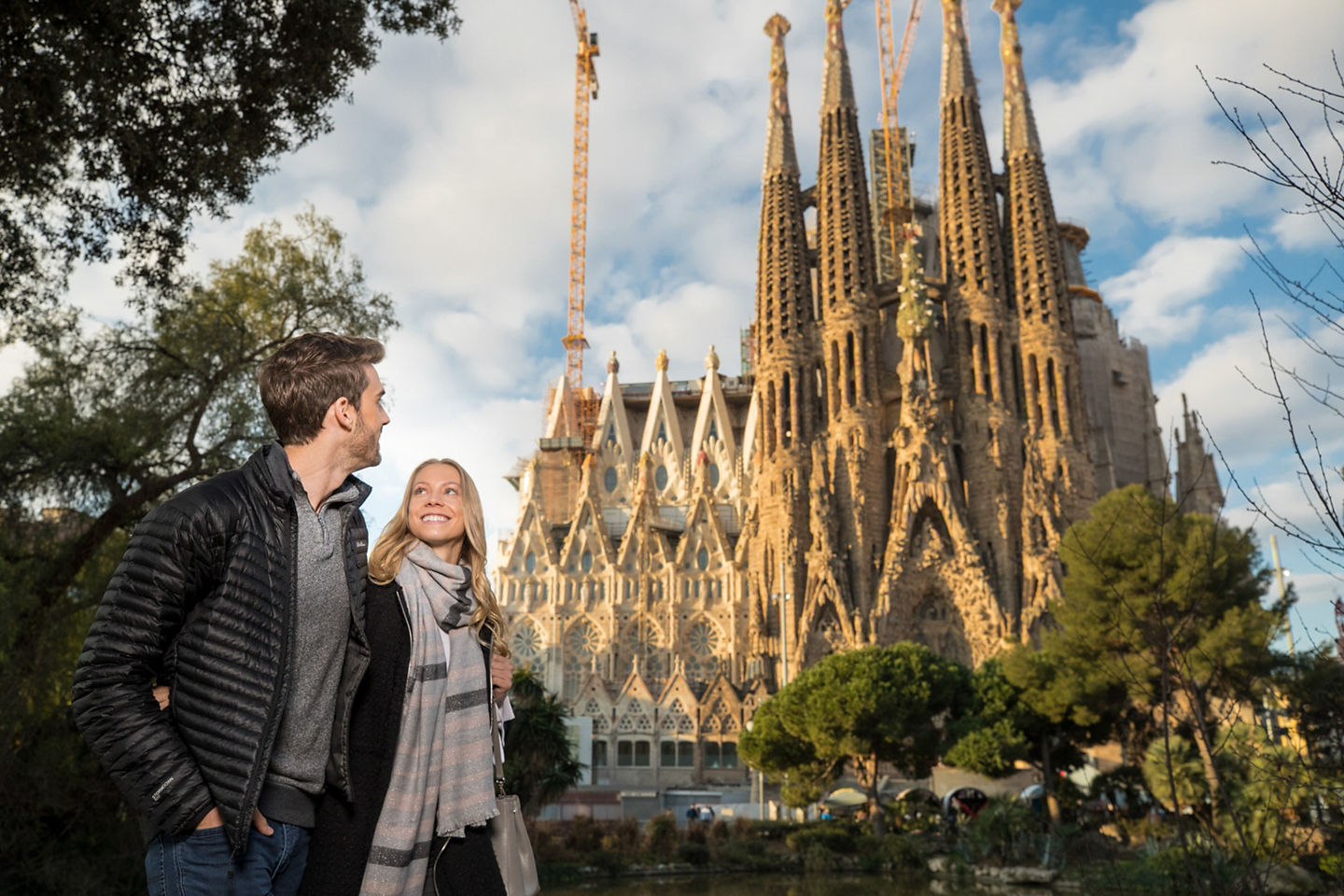 A couple walks near La Sagrada Família, its towering spires rising above Barcelona’s city streets. - Barcelona, Spain