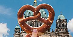 The girl is holding a delicious traditional German pretzel in the hand against the backdrop of the Berlin Cathedral is called Berliner Dom. Berlin, Germany