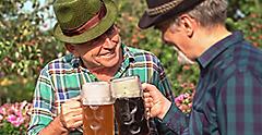 Men with beer mugs with Bavarian beer in Tyrolean hats with feathers celebrating beer festival outdoor among the trees in Germany