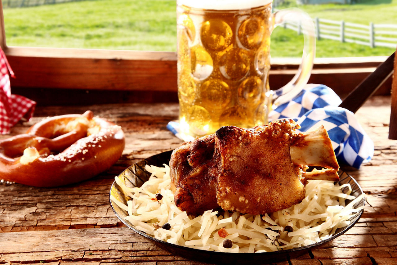 Roasted pork knuckle or hock with a crispy golden rind served with a pretzel and cold beer at a tavern offering traditional Bavarian cuisine to tourists