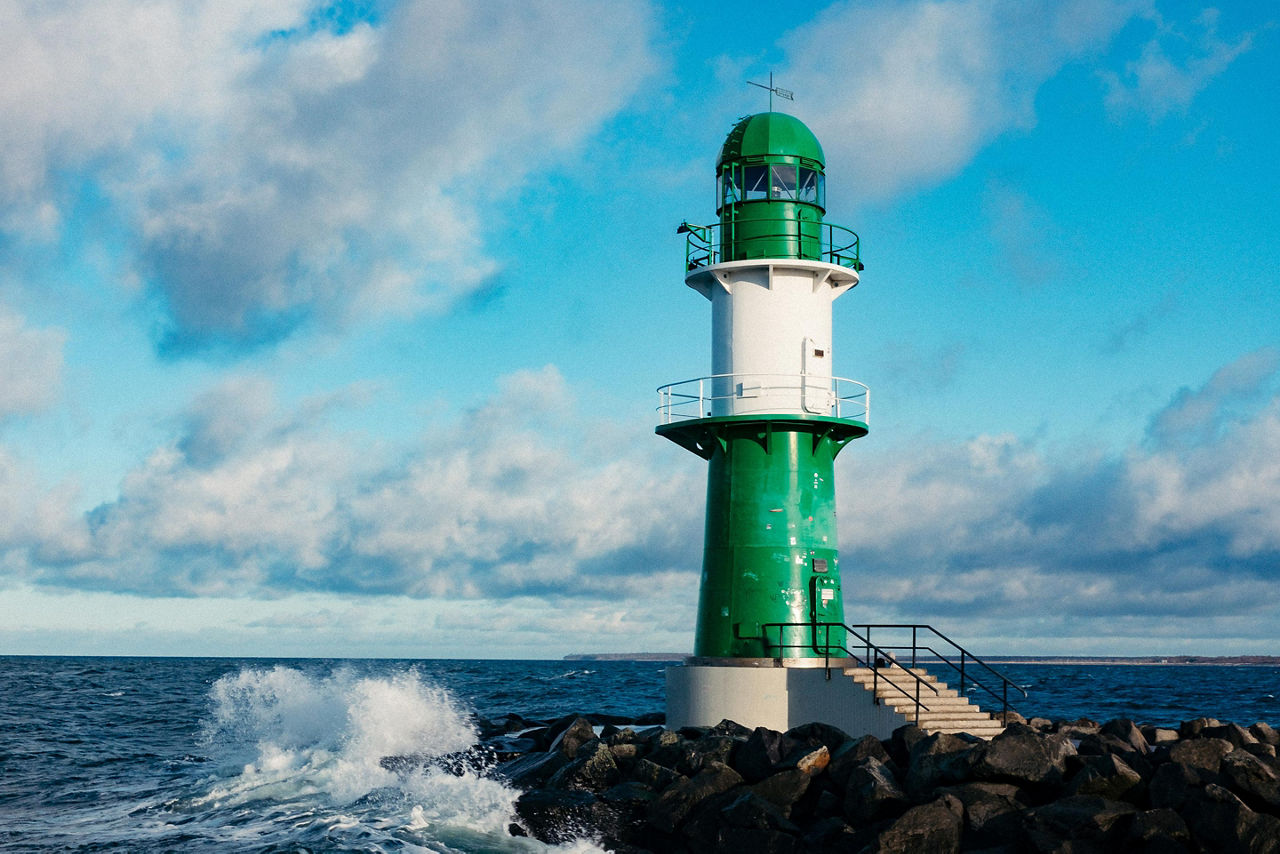 A green and white lighthouse with waves crashing against the rock jetty