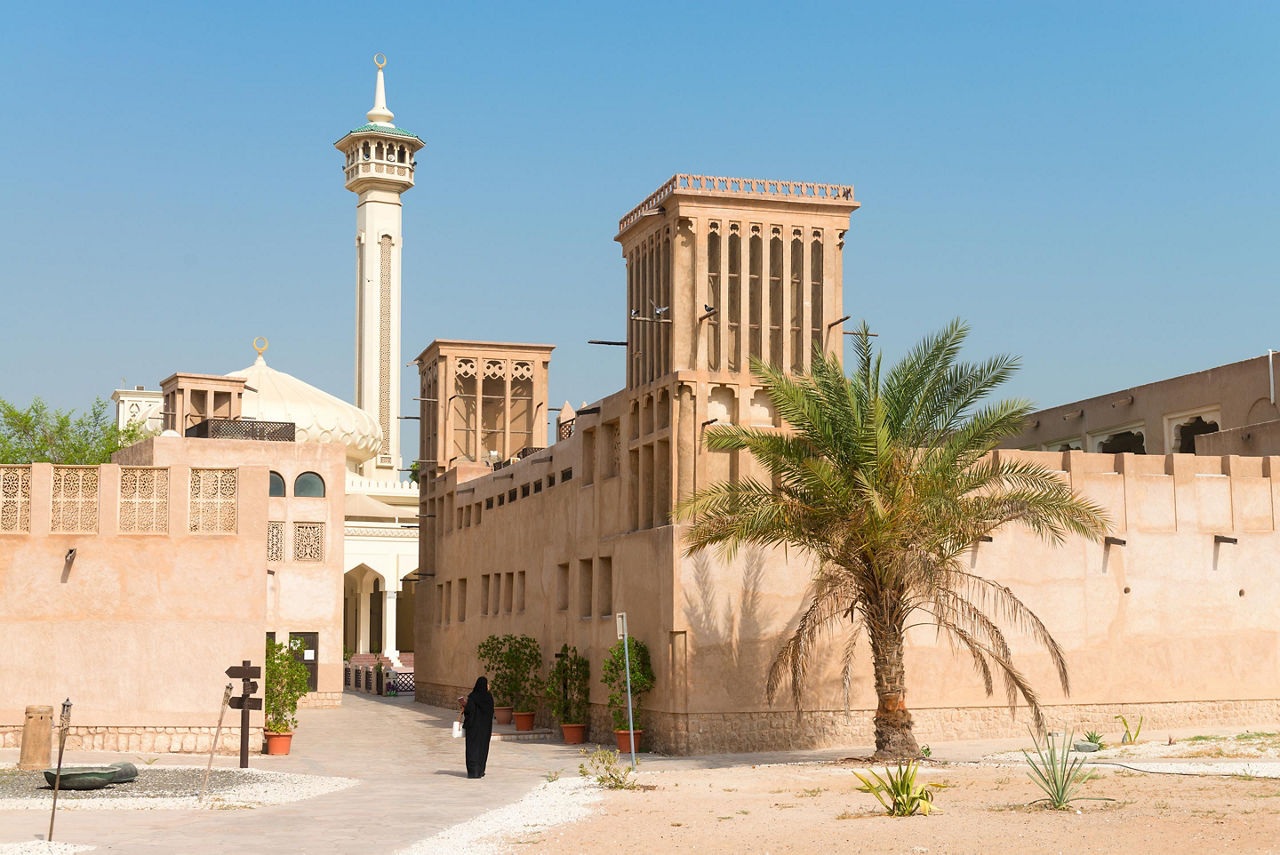 Woman in traditional muslim black dress in old arabic city district with mosque minaret in Al Fahidi Historical District of Dubai