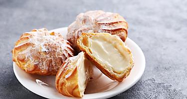 Four profiteroles cream pastries on a white plate