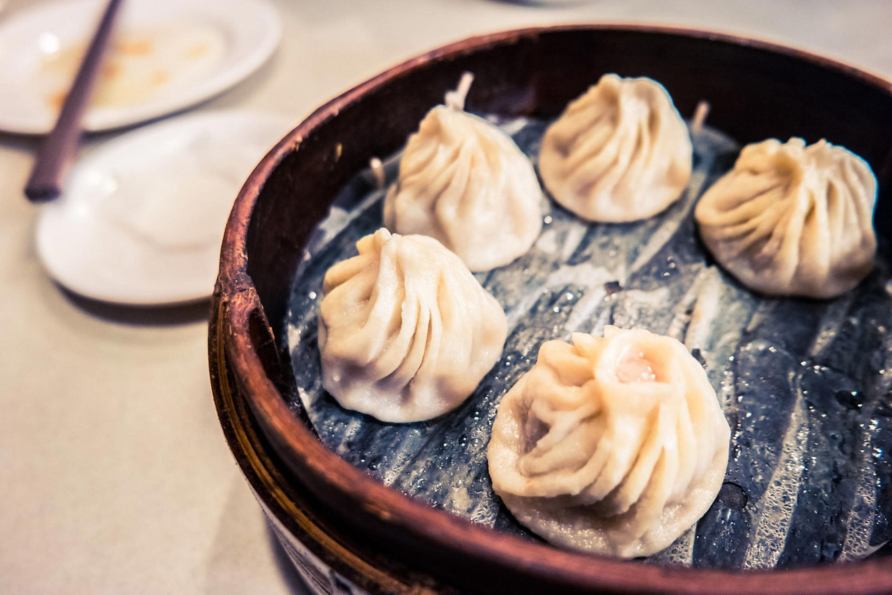 Traditional Taiwan food is steamed dumplings served on a table in a wooden dish with chopsticks