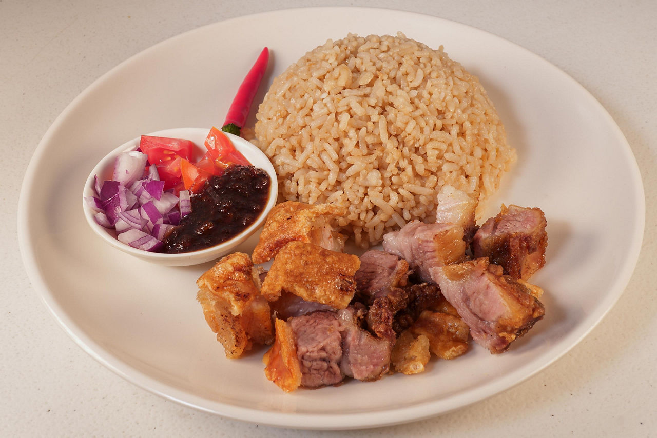 Crispy bagnet, a deep fried crispy pork belly dish, served with onion and fresh tomatoes and a side of rice, in Ilocos, Philippines
