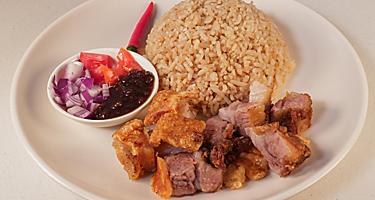 Crispy bagnet, a deep fried crispy pork belly dish, served with onion and fresh tomatoes and a side of rice, in Ilocos, Philippines