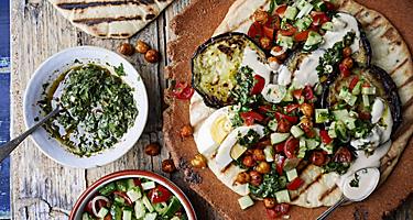 A warm toasted pita bread topped with eggplant, tzaziki sauce, and israeli salad
