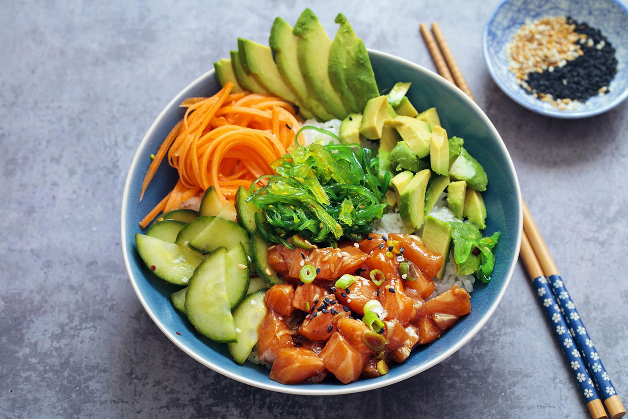 Poke bowl filled with rice, avocado, seaweed salad, veggies, and raw salmon