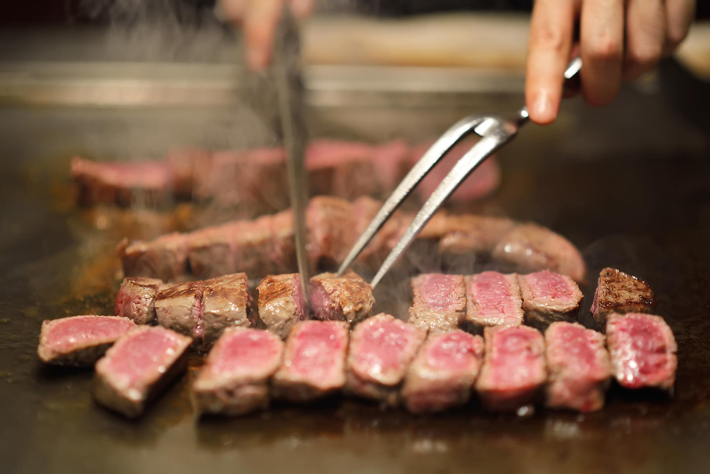 Kobe beef sizzles on a hot grill, with rich marbling browning at the edges. - Kobe, Japan