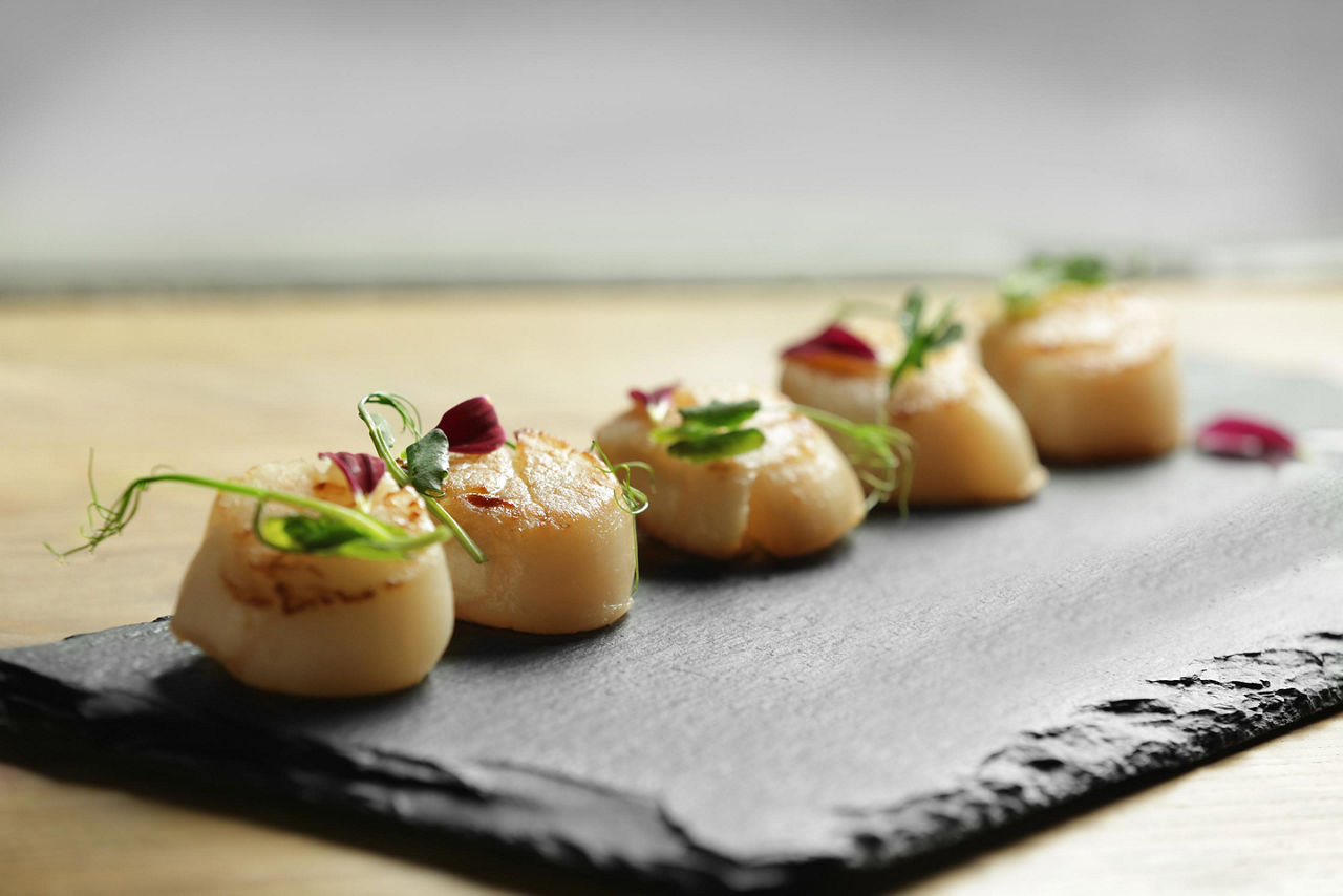 Five scallops on a black plate with garnish